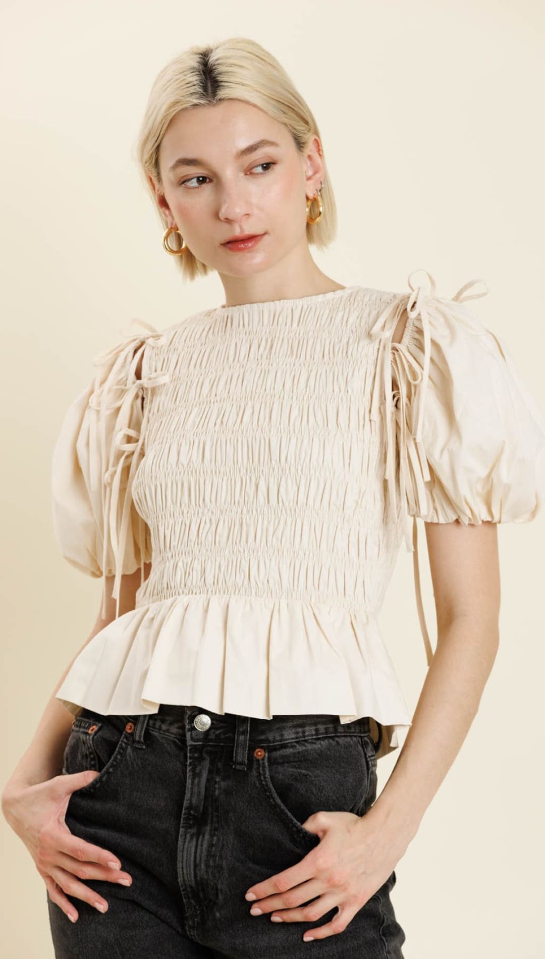 A cream-colored, smocked peplum top with puffed sleeves and shoulder ties.