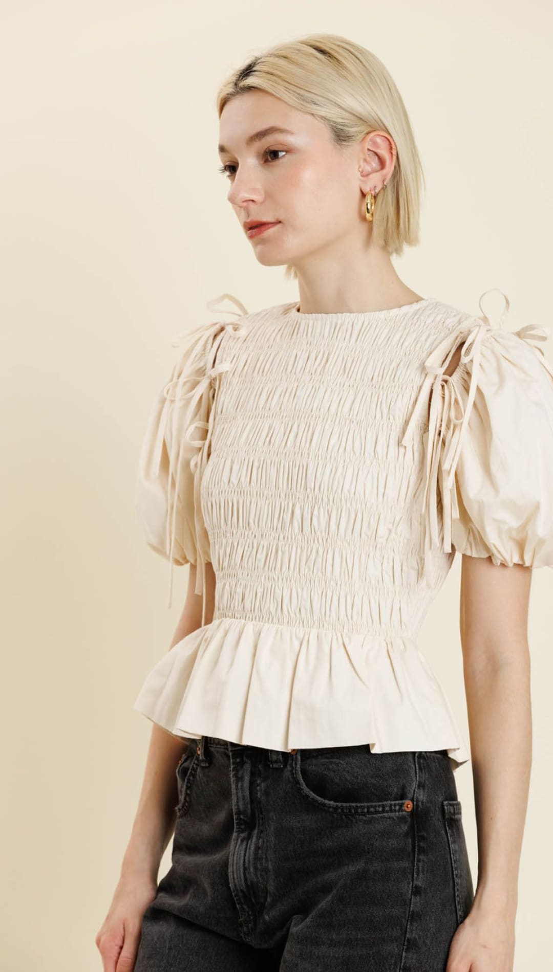 A light-colored, smocked peplum top with puffed sleeves and shoulder ties.