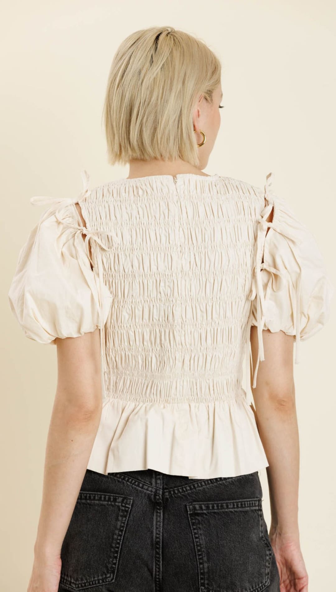 A woman’s off-white smocked peplum top with puff sleeves and tie details on the shoulders.