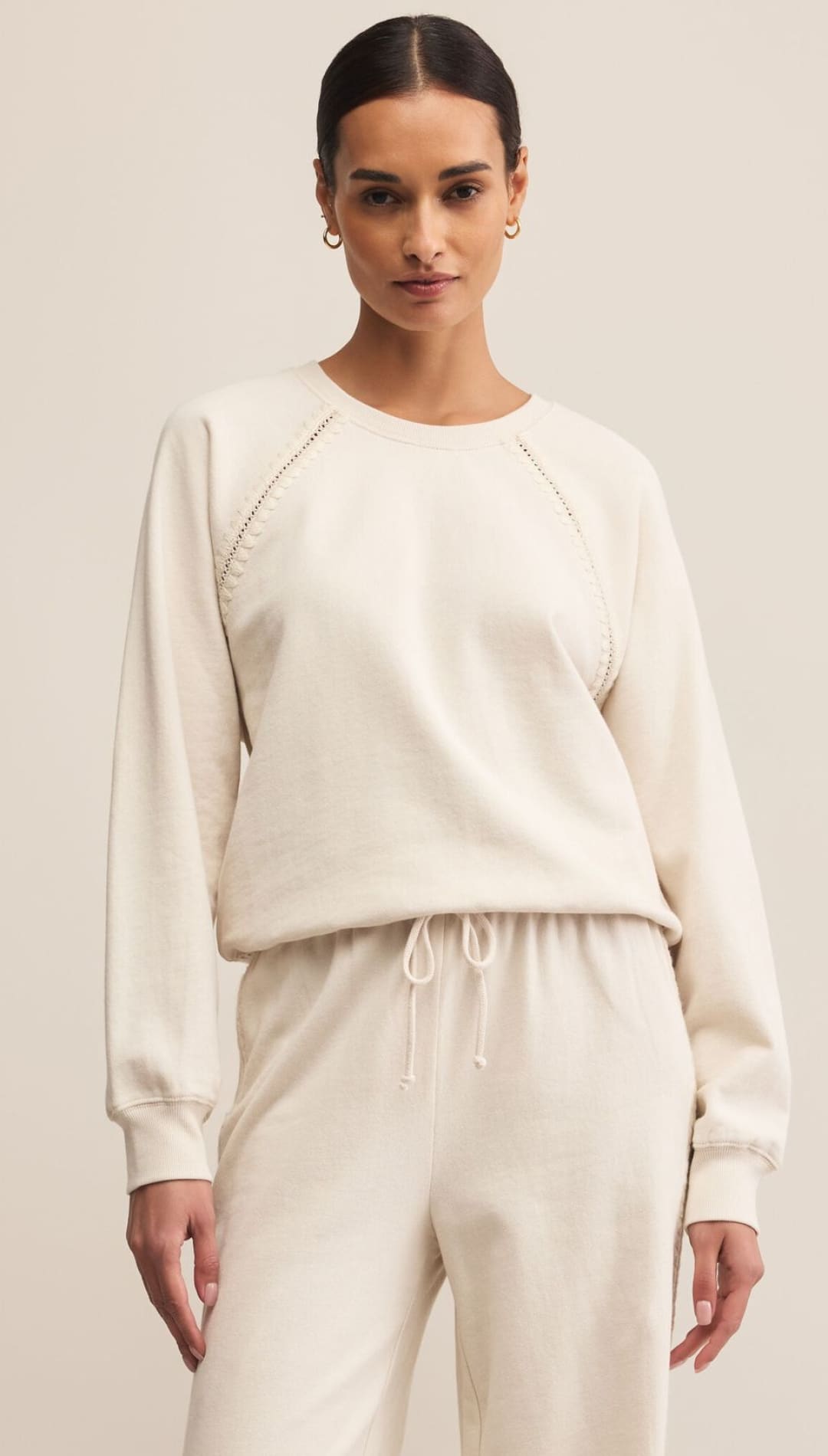 Cream-colored sweatshirt with long sleeves and drawstring waistband, featuring a relaxed fit.