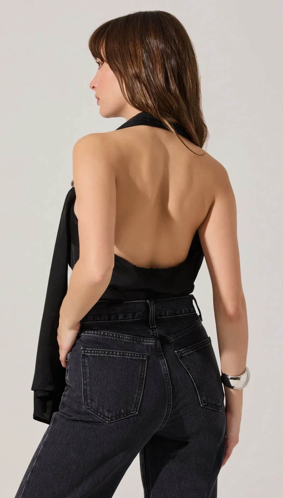 Woman wearing a black halter top with an open back and dark wash jeans.