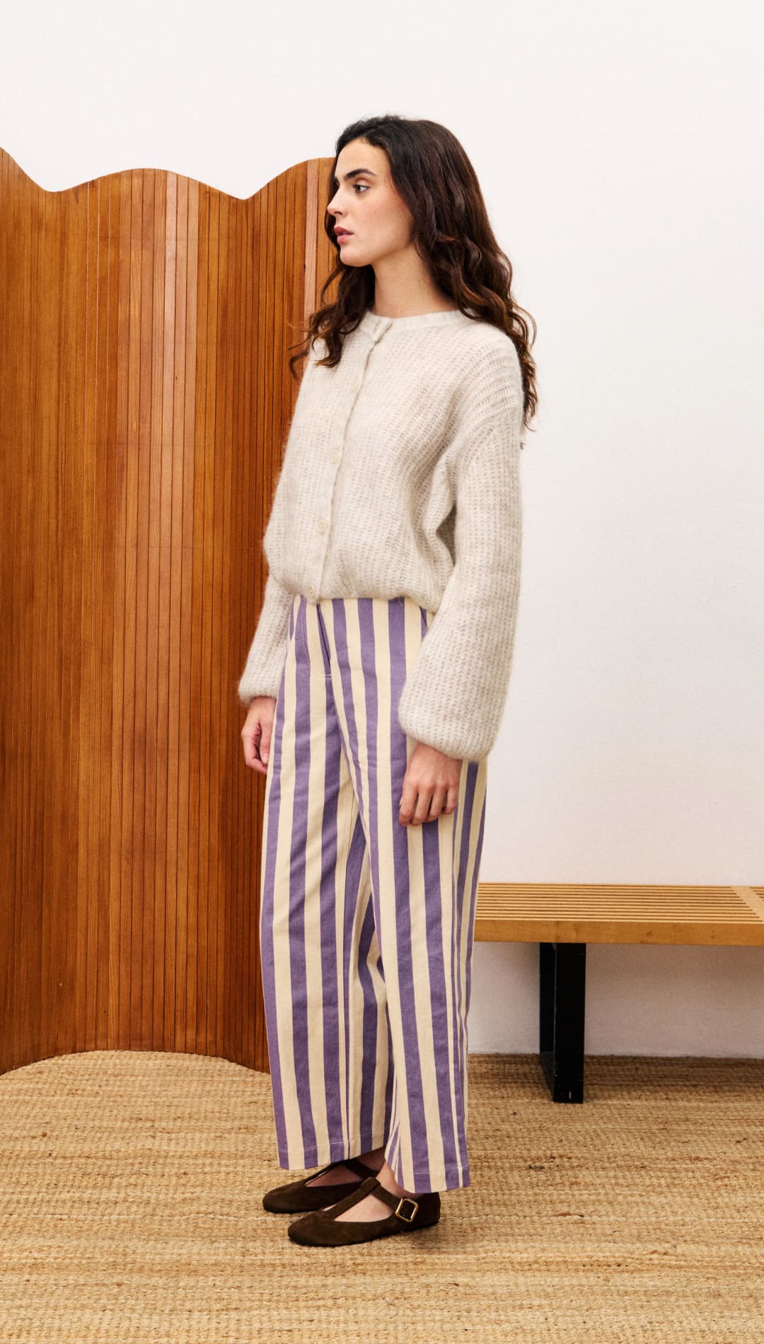 Woman wearing a cream-colored fuzzy cardigan, purple and white striped wide-leg pants, and dark brown Mary Jane flats.