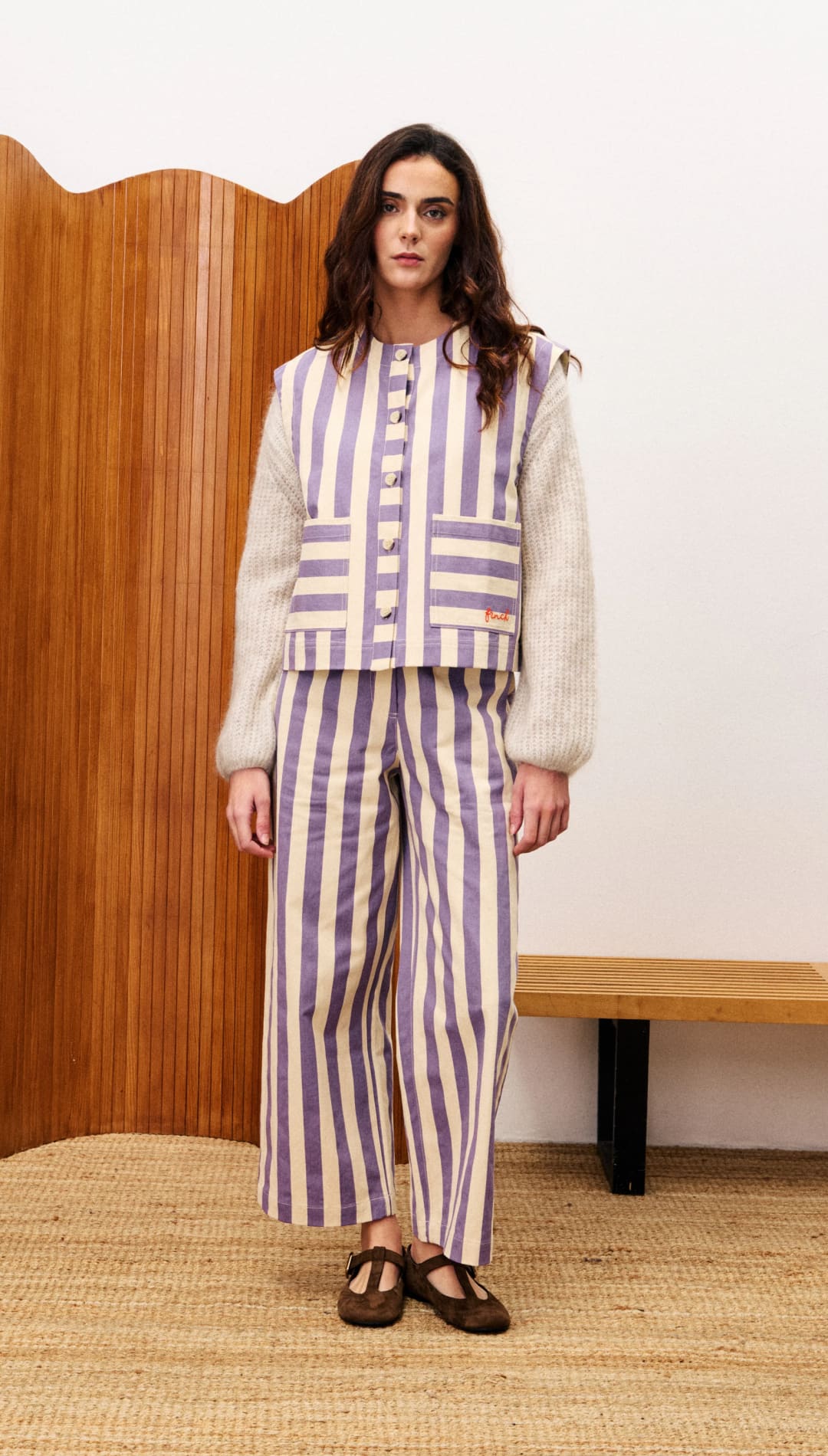 Woman wearing a striped lavender and beige coordinated set with a light grey long-sleeved top and brown Mary Jane shoes.