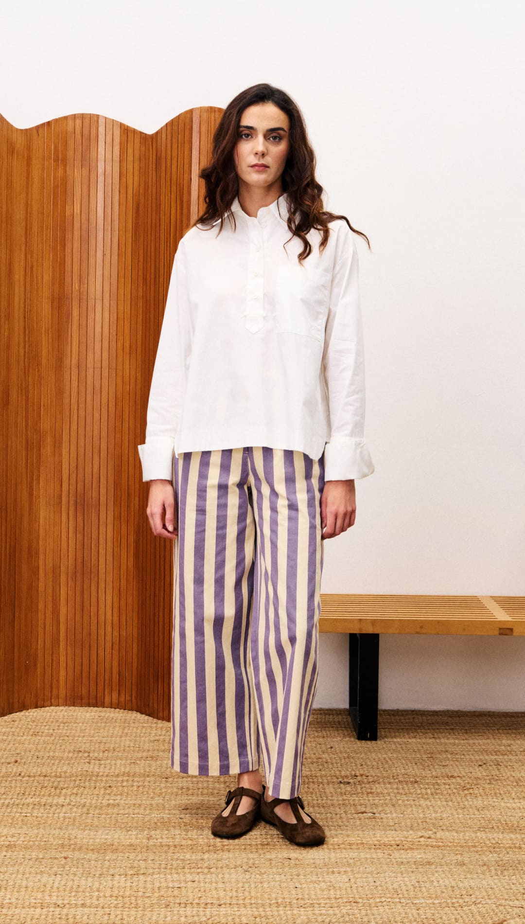 A woman wearing a white collared shirt, purple and beige striped wide-leg pants, and brown Mary Jane shoes.