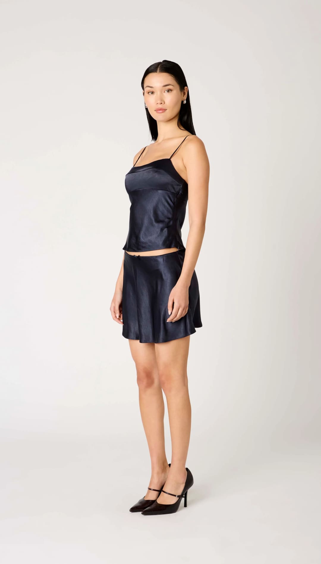 A woman modeling a two-piece navy blue satin camisole and mini skirt set.