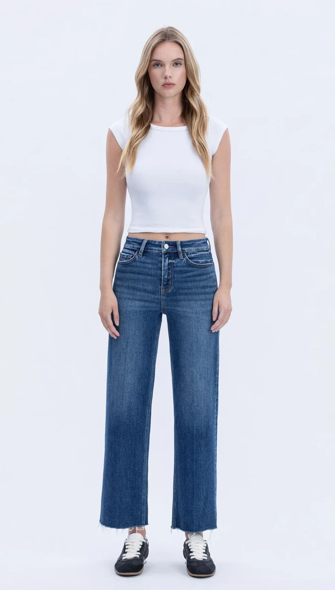 Women’s white cap-sleeve crop top with distressed wide-leg blue jeans and black and white sneakers.