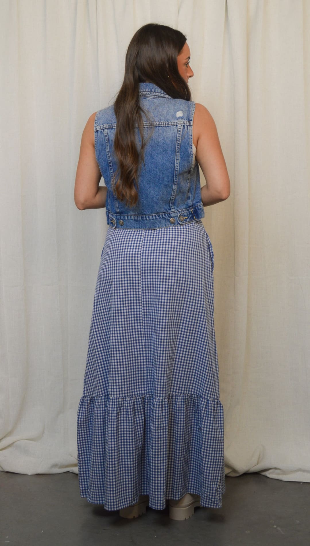 Woman in denim vest and gingham dress.