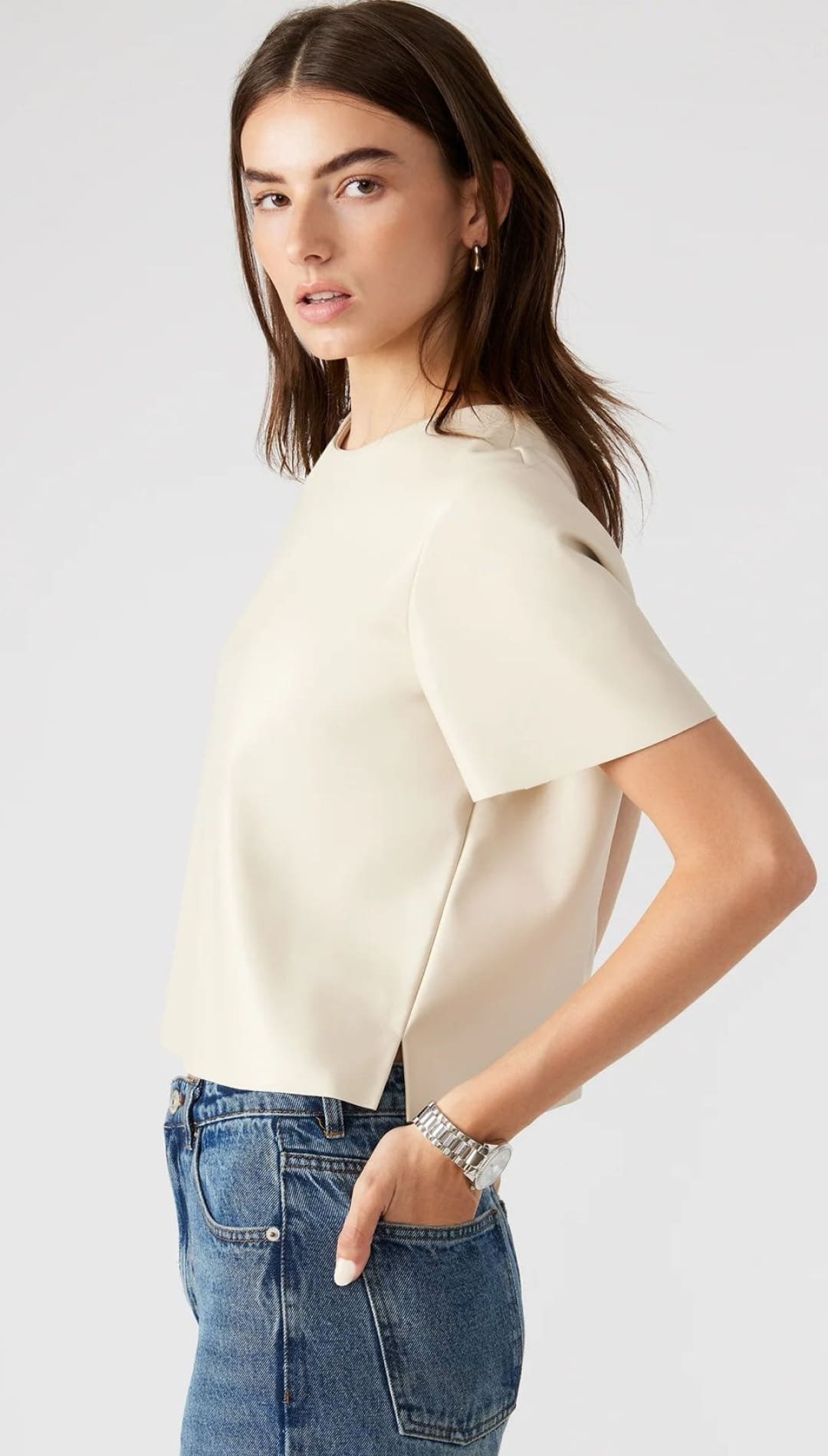 A woman wearing a light-colored short-sleeved top and blue jeans, with a silver watch on her left wrist.