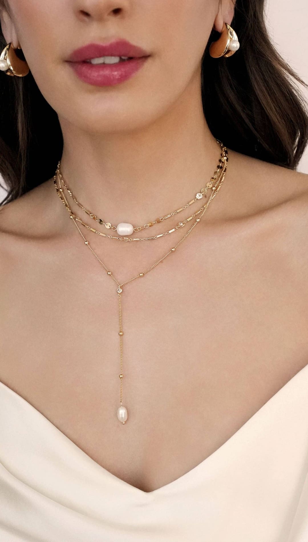 Woman wearing layered gold necklaces with pearl accents.