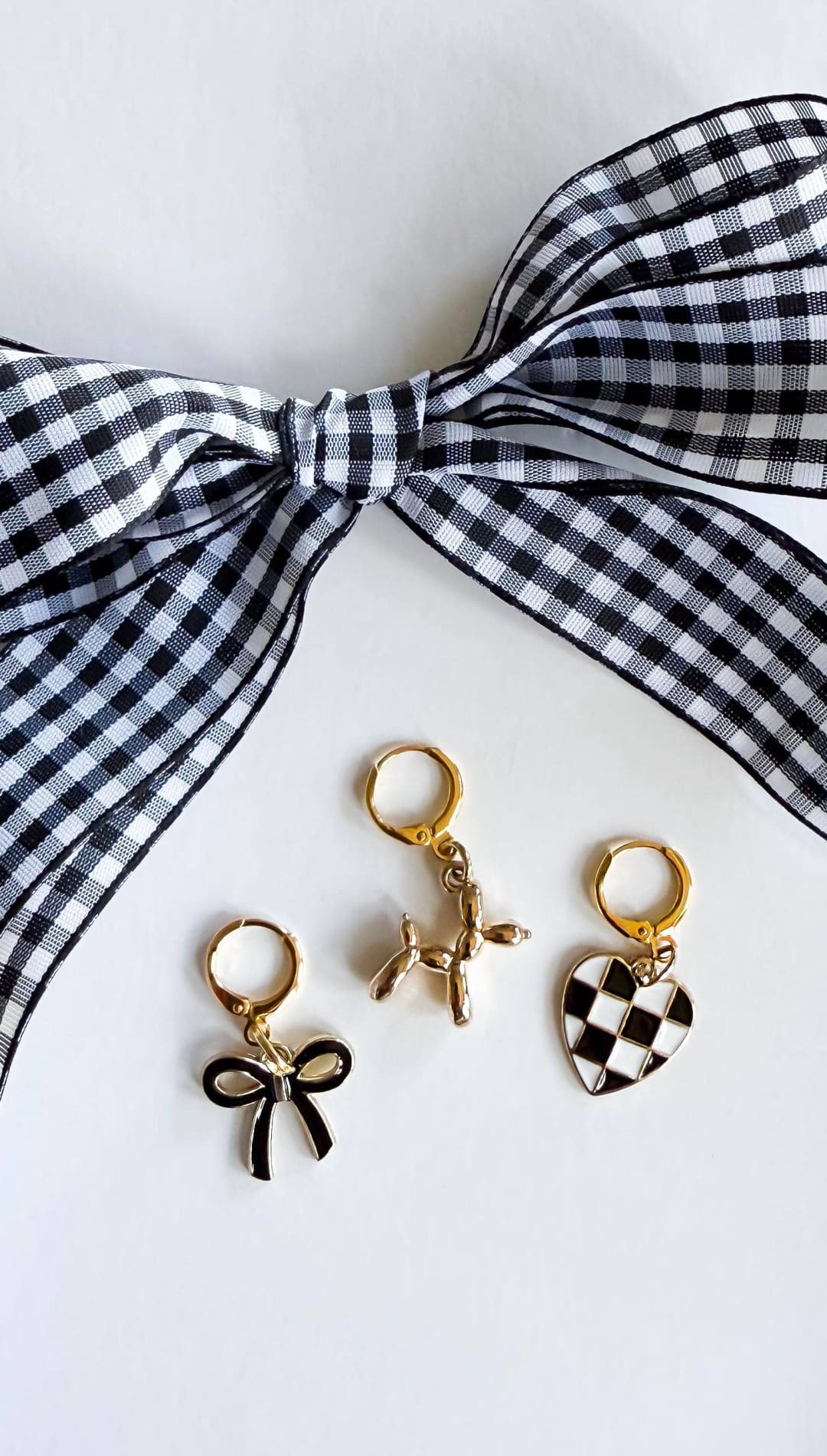 Three gold earrings with charms and a black and white checkered bow.