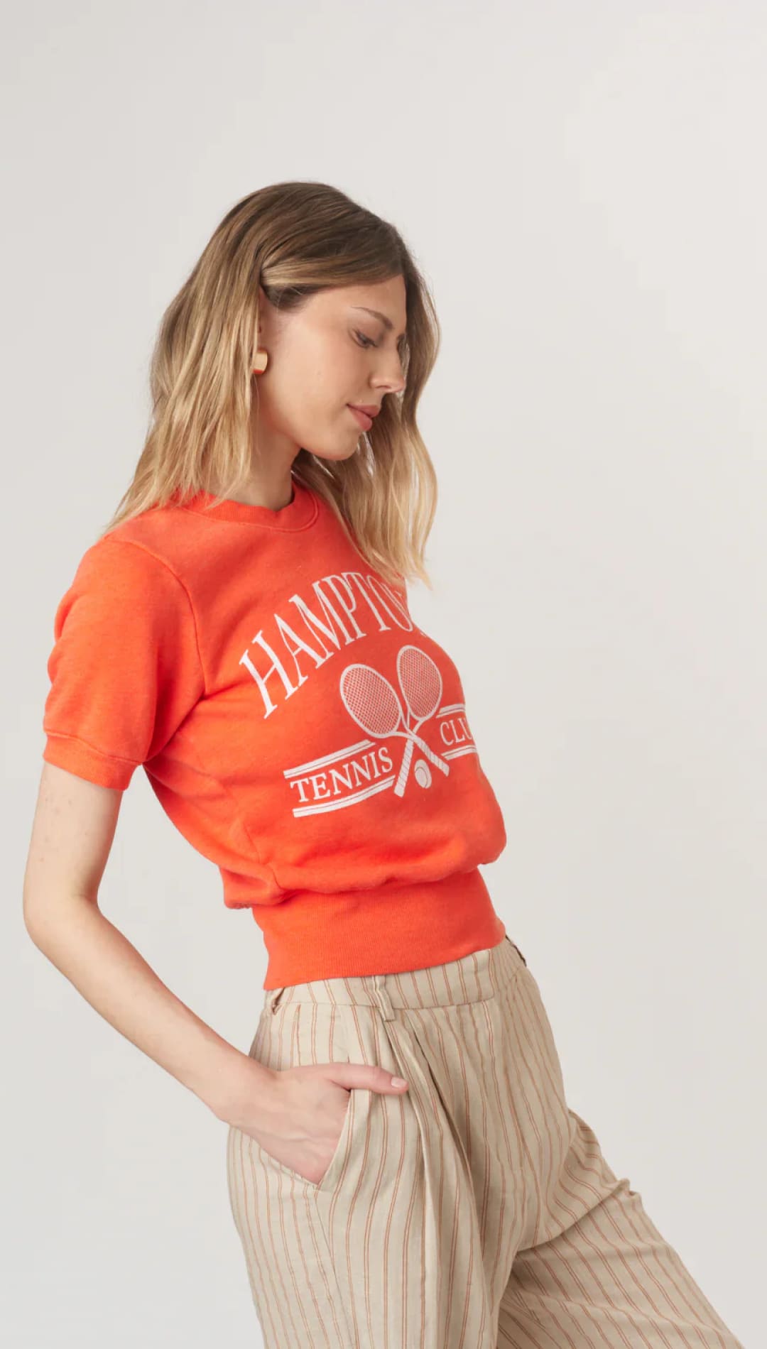 Woman’s orange tennis-themed top and striped pants.