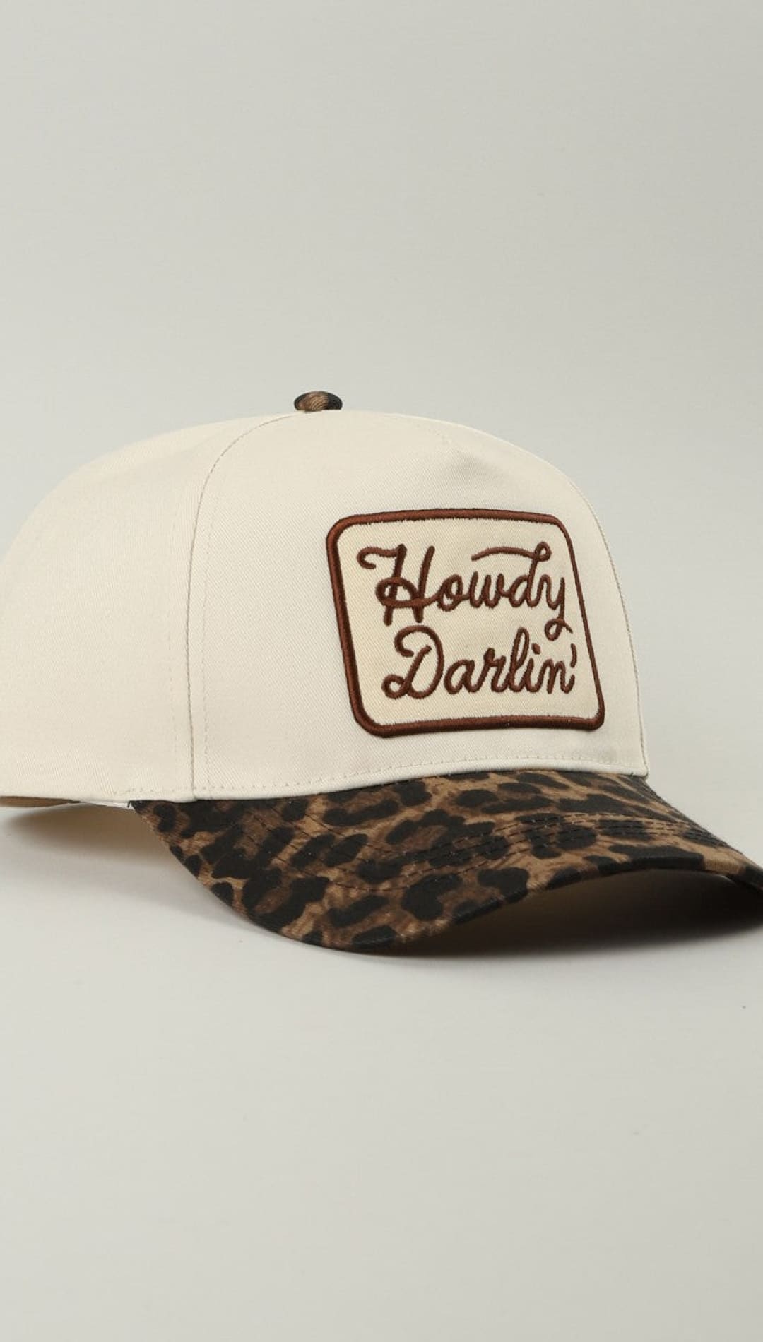 Leopard print baseball cap with ’howdy darlin’ embroidered in brown on a cream-colored panel.