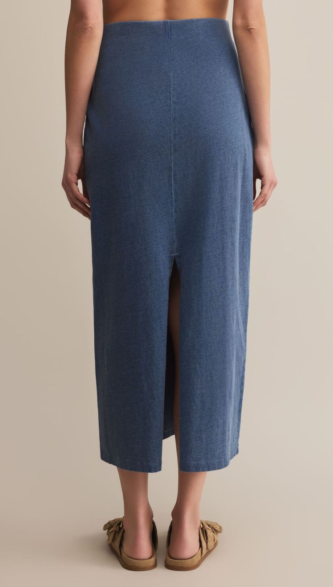A long, flowing denim-blue skirt with a back slit, paired with tan flat sandals.