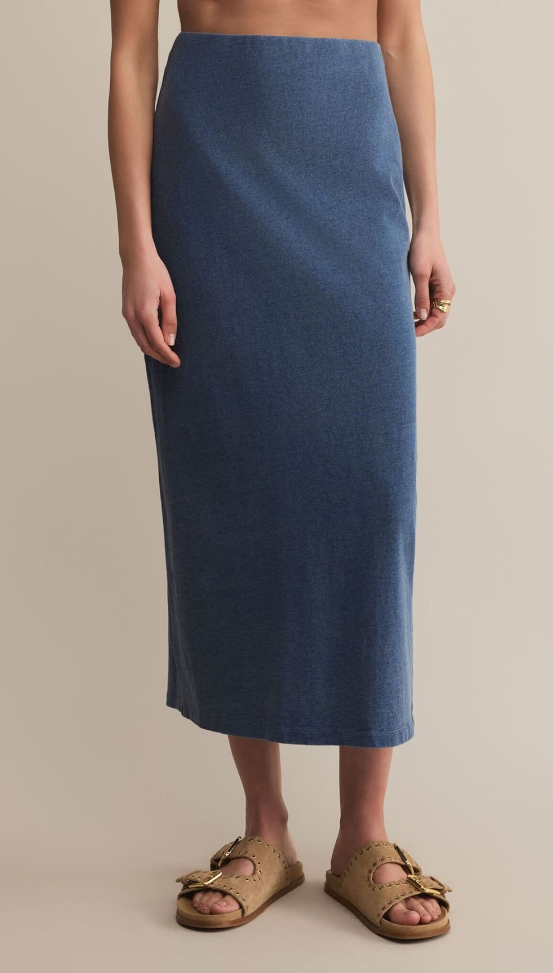 A mid-length, fitted denim-blue skirt with a straight hem, paired with light brown, double-buckle slide sandals.