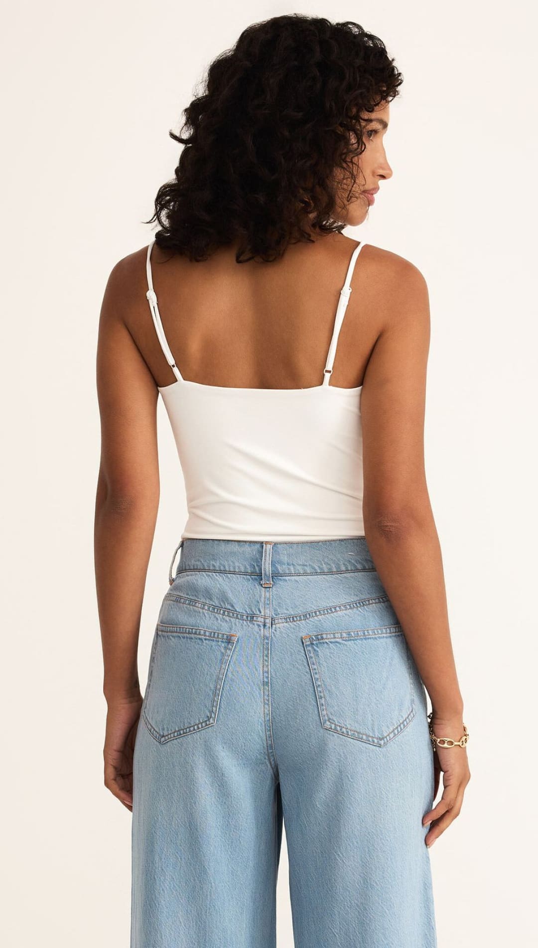 Woman wearing a white tank top and light blue jeans.