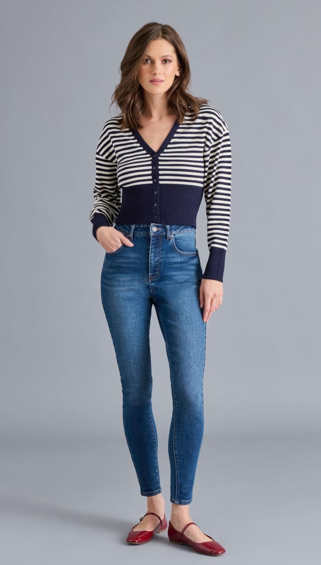 A woman wearing a striped cropped cardigan, high-waisted skinny jeans, and red ballet flats.