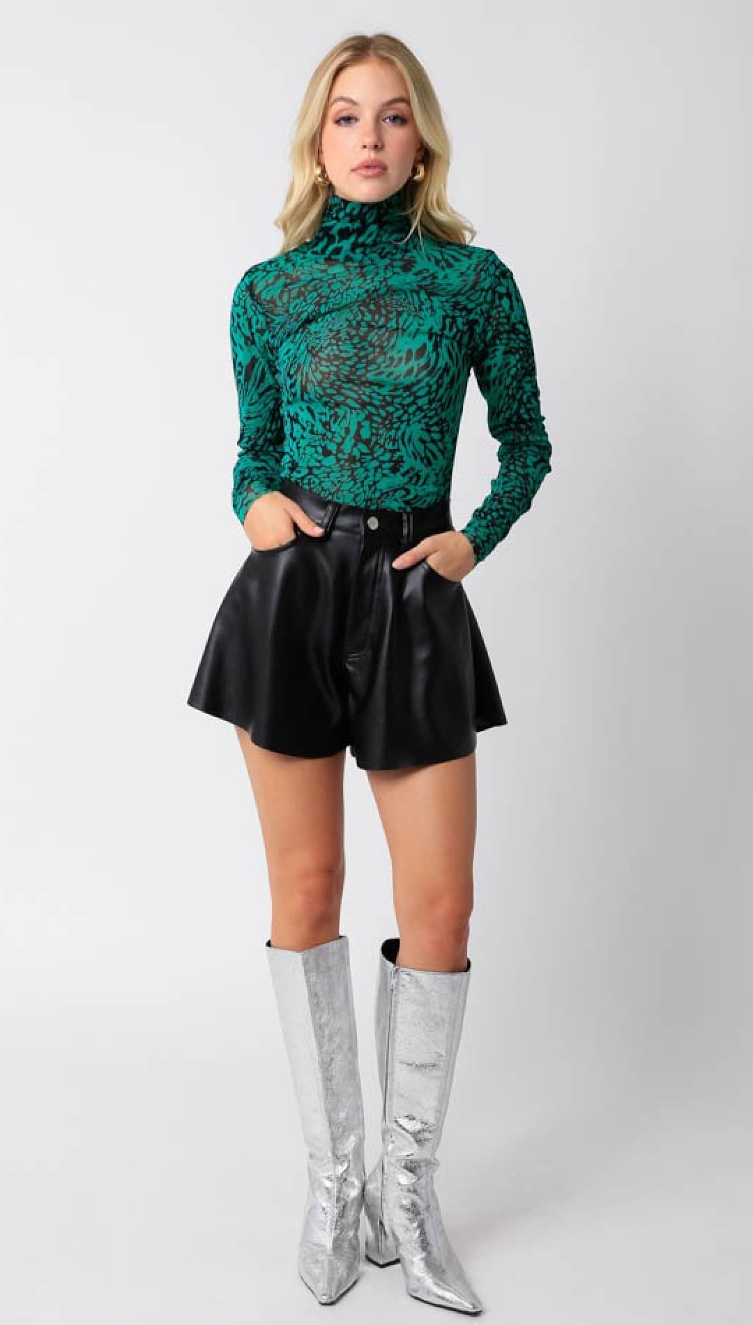 Green and black long-sleeve turtleneck top with black faux leather shorts and silver knee-high boots.