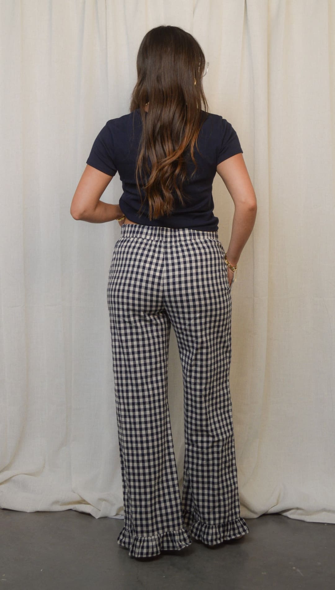 A woman wearing a dark blue short-sleeved top and black and white gingham wide-leg pants with ruffled hems.