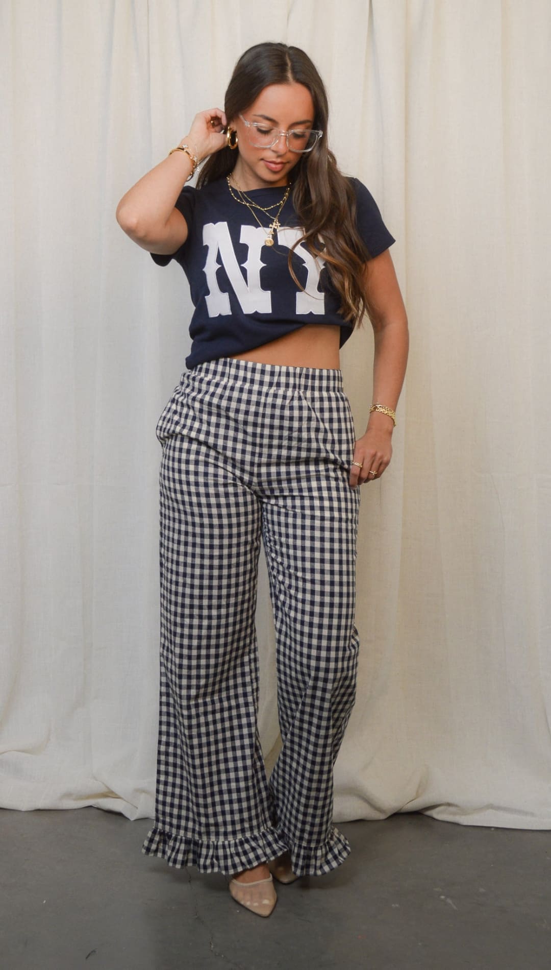 A woman wearing a dark blue New York-themed crop top and black and white gingham wide-leg pants with ruffled hems.