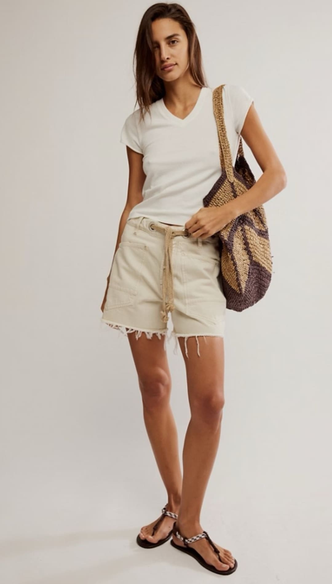 Woman wearing a white v-neck t-shirt, beige shorts, and sandals.