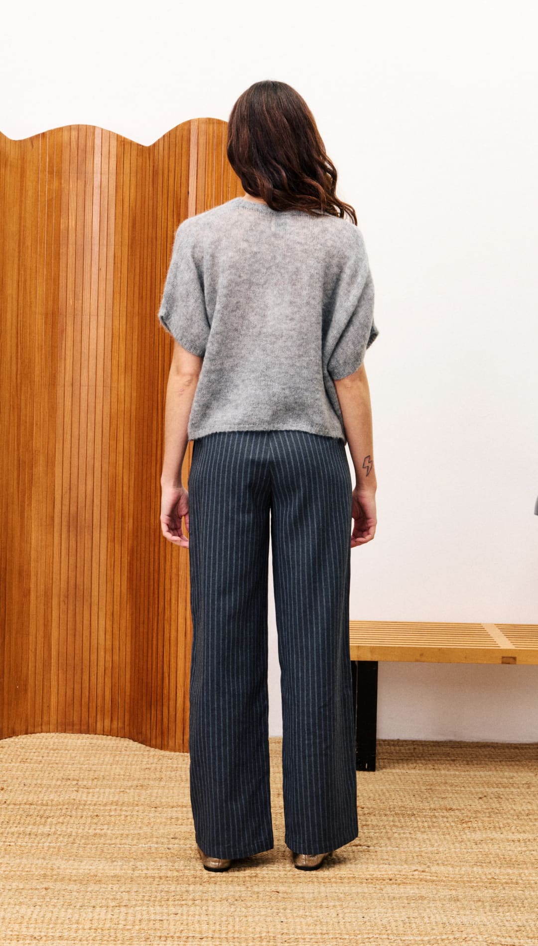A woman modeling a loose-fitting gray short-sleeved top and dark pinstriped wide-leg trousers.
