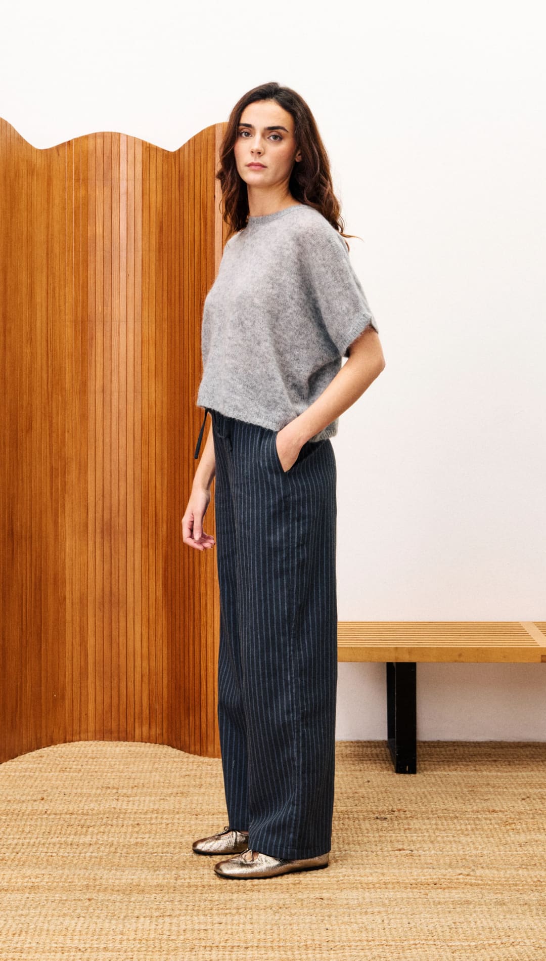 Woman in a loose-fitting gray short-sleeved top and dark pinstriped wide-leg pants.