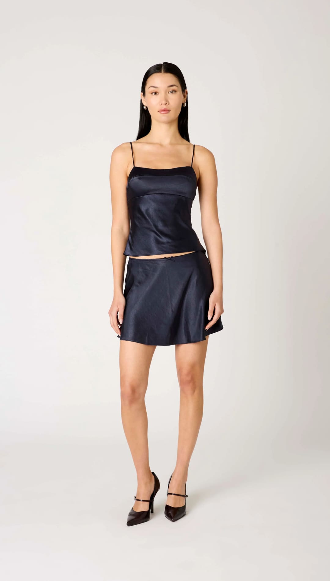A woman in a navy blue satin camisole and matching mini skirt with black high heels.