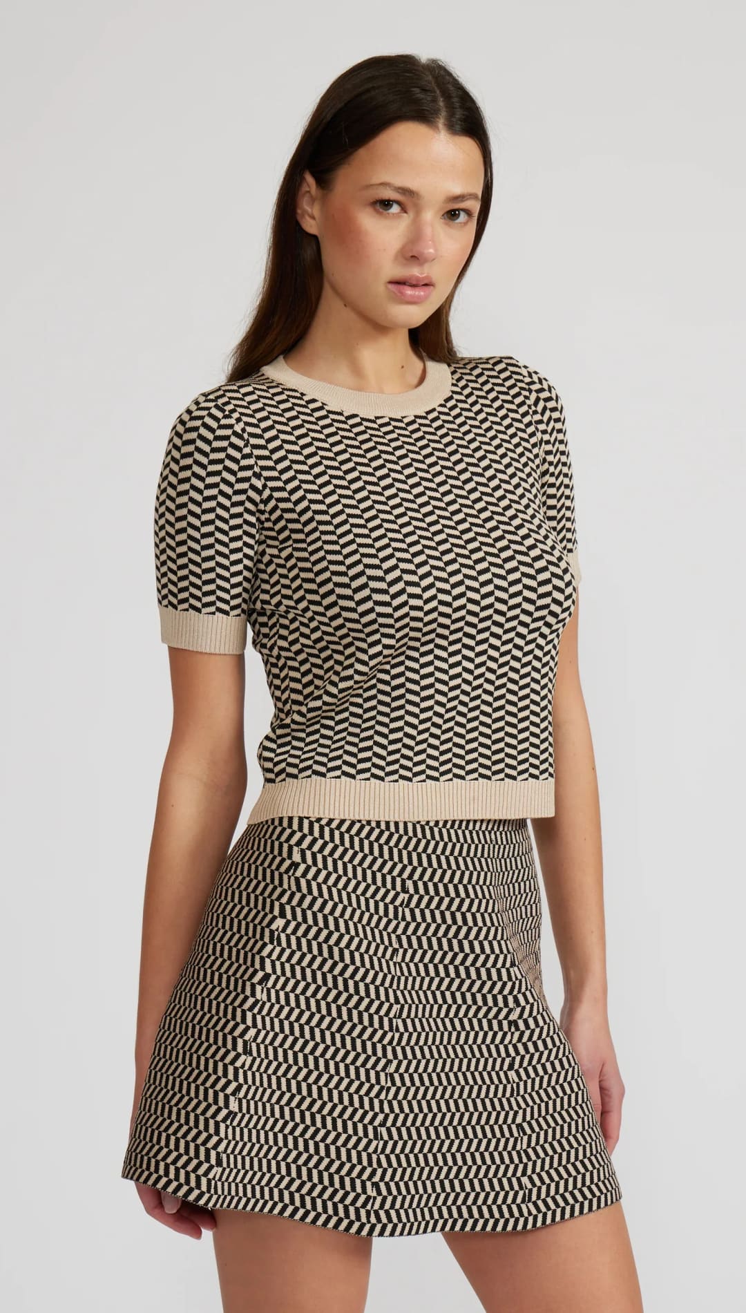 A two-piece knitted set featuring a short-sleeved top and a mini skirt, both with a black and beige chevron pattern.