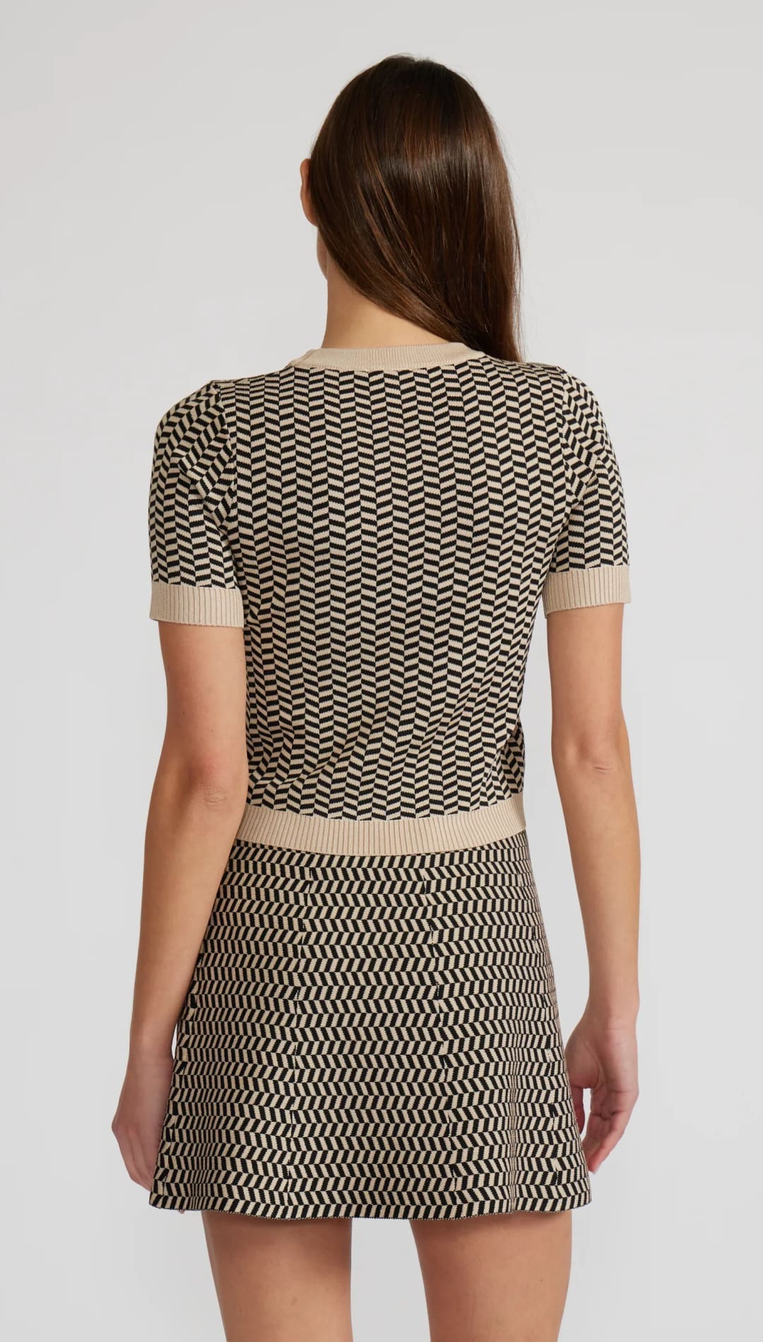 A woman wearing a beige and black chevron knit two-piece outfit with a short-sleeved top and a mini skirt.