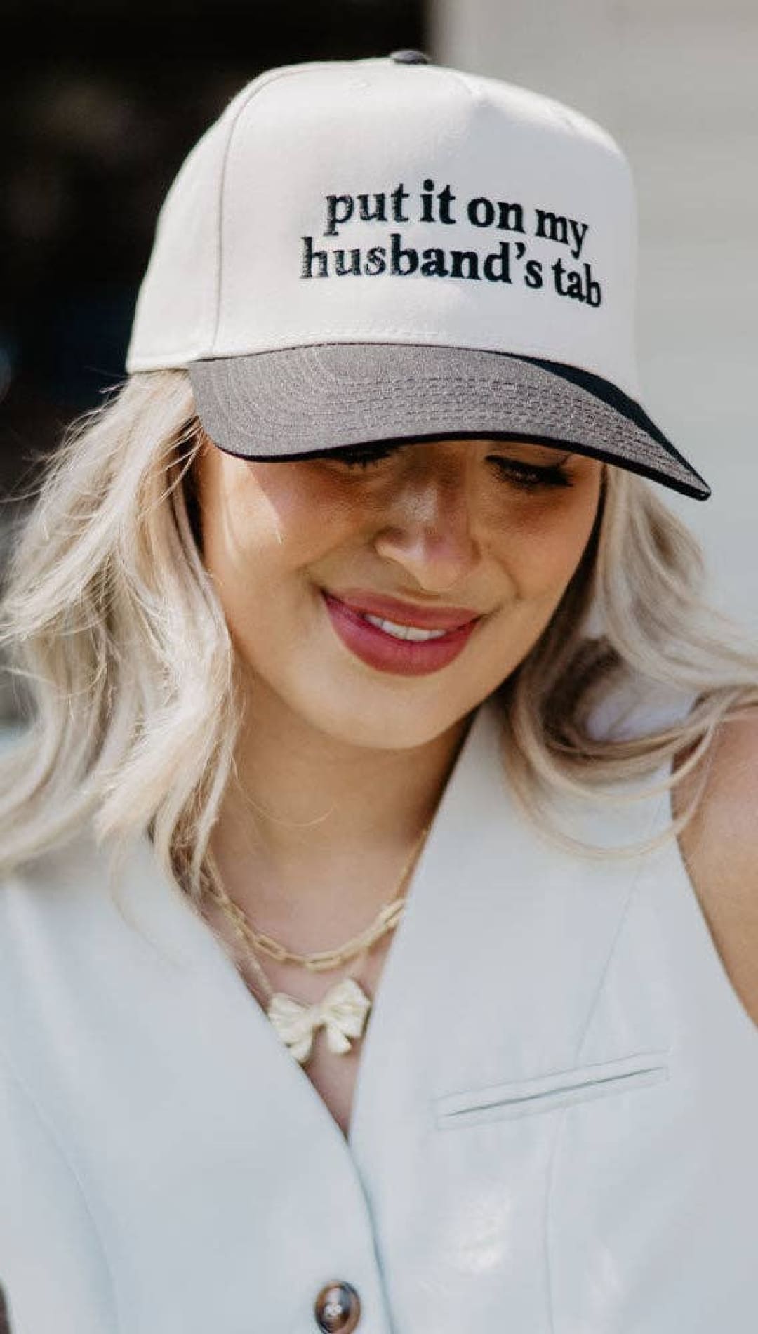 White baseball cap with black text ’put it on my husband’s tab’