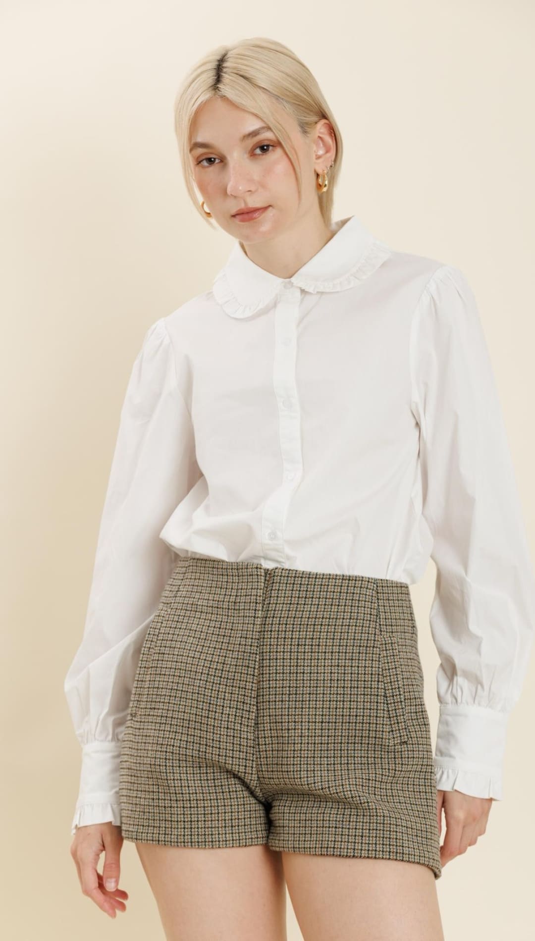 A white collared shirt with puffy sleeves and olive green plaid shorts.
