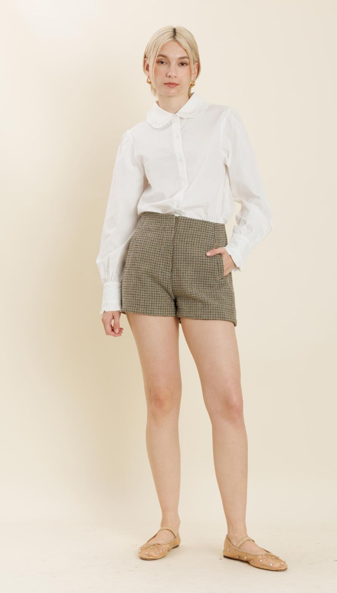A woman modeling a white long-sleeve blouse, brown plaid shorts, and nude ballet flats.