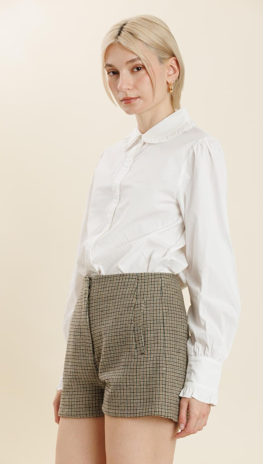 A woman’s white long-sleeved collared shirt with brown checkered shorts.