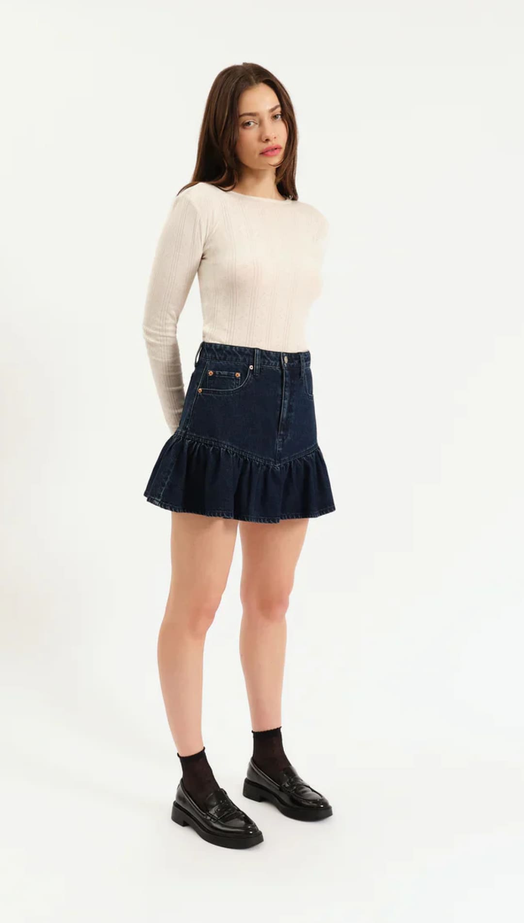 Denim ruffled mini skirt with black patent leather shoes and white long-sleeve top.
