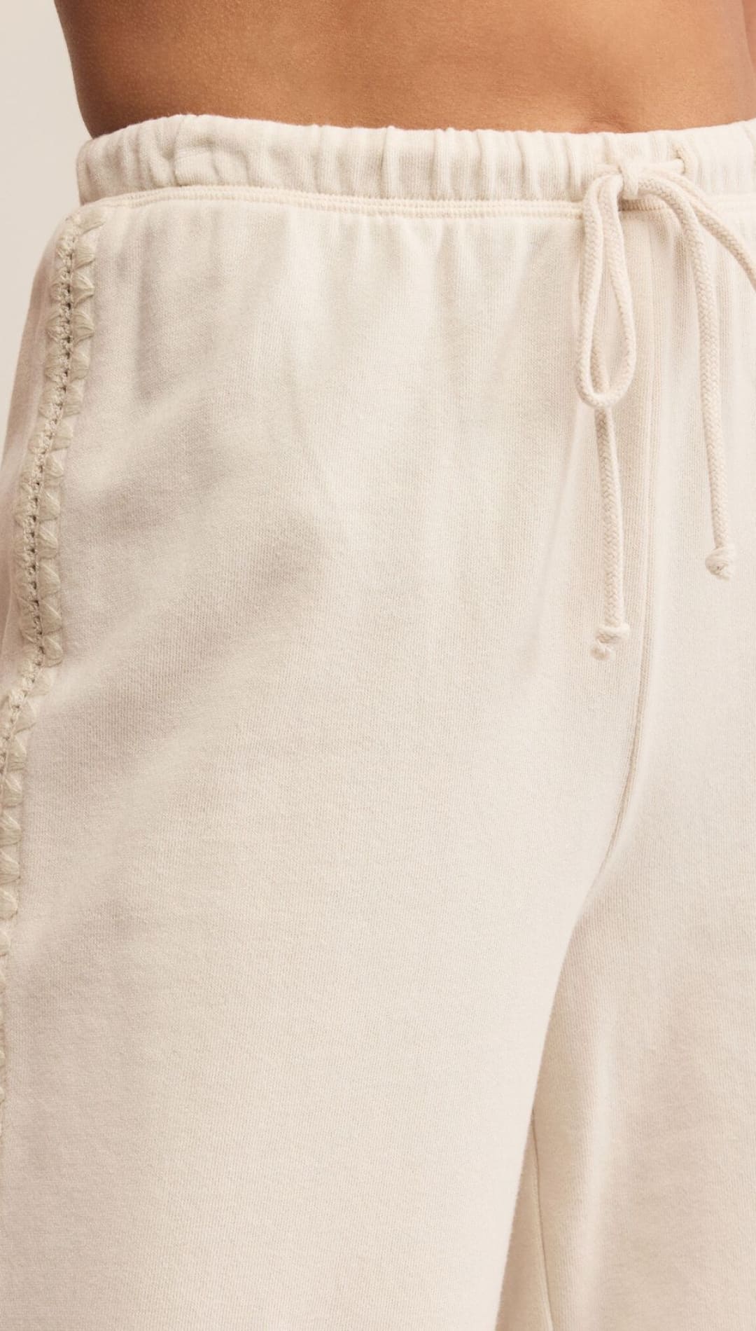 Cream-colored drawstring pants with decorative stitching along the side.