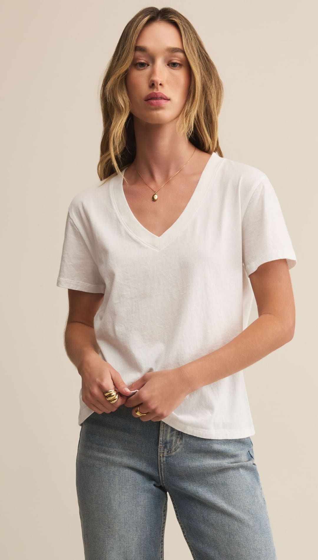 A woman wearing a white short-sleeved V-neck t-shirt and light blue jeans.