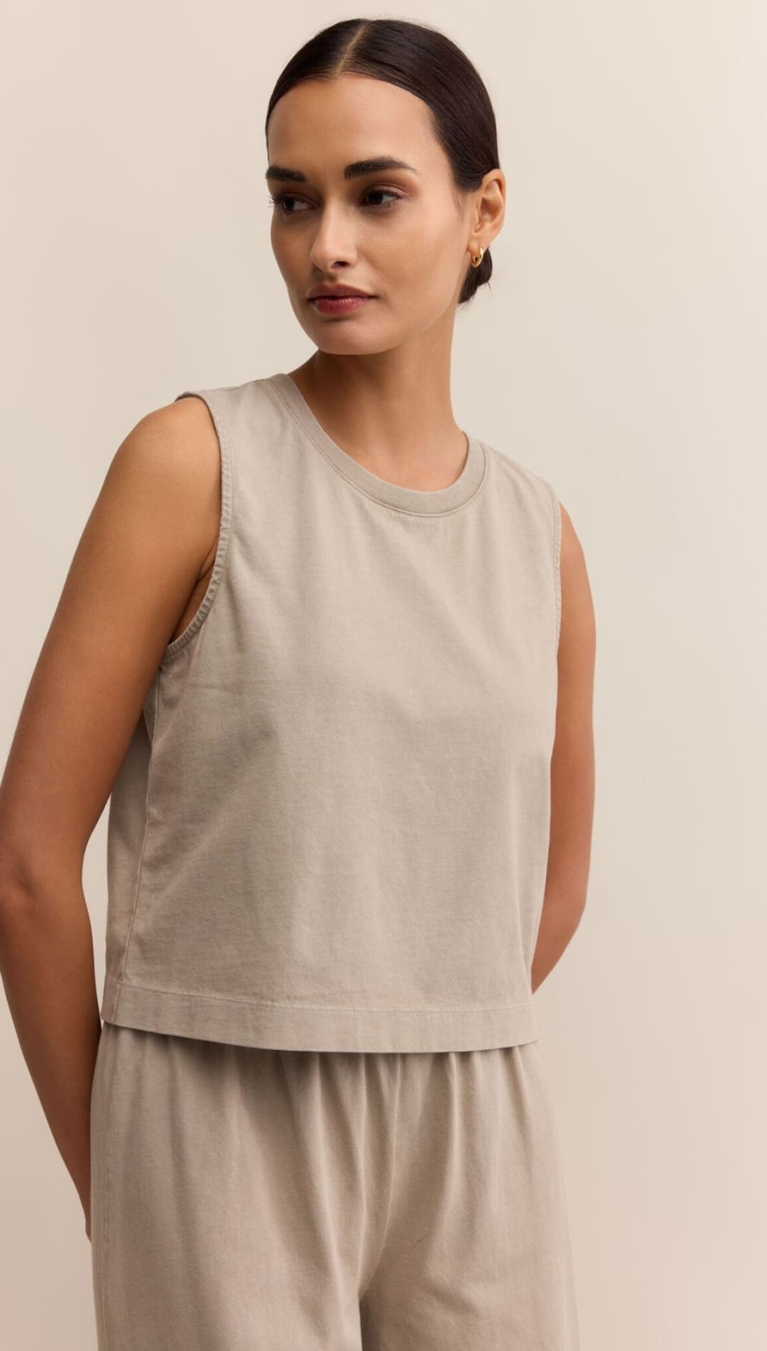 A woman wearing a light beige sleeveless crop top and matching relaxed-fit pants.