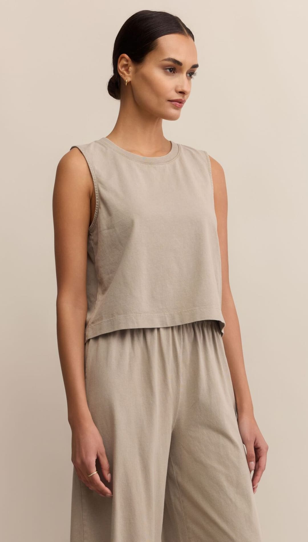 A woman wearing a light taupe, sleeveless top and wide-leg pants.