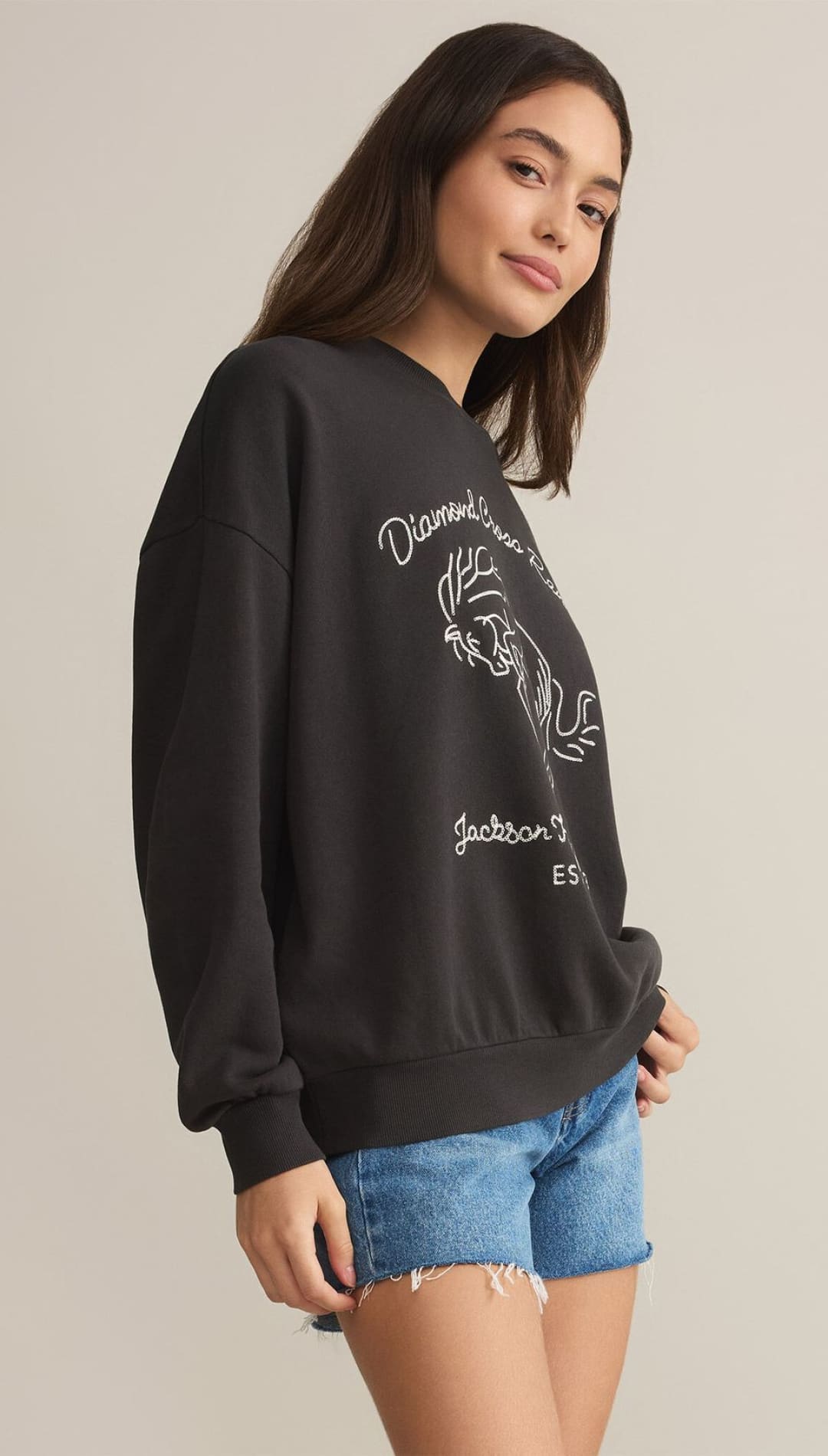 A dark gray, oversized crewneck sweatshirt with a white line drawing of a rooster and text.