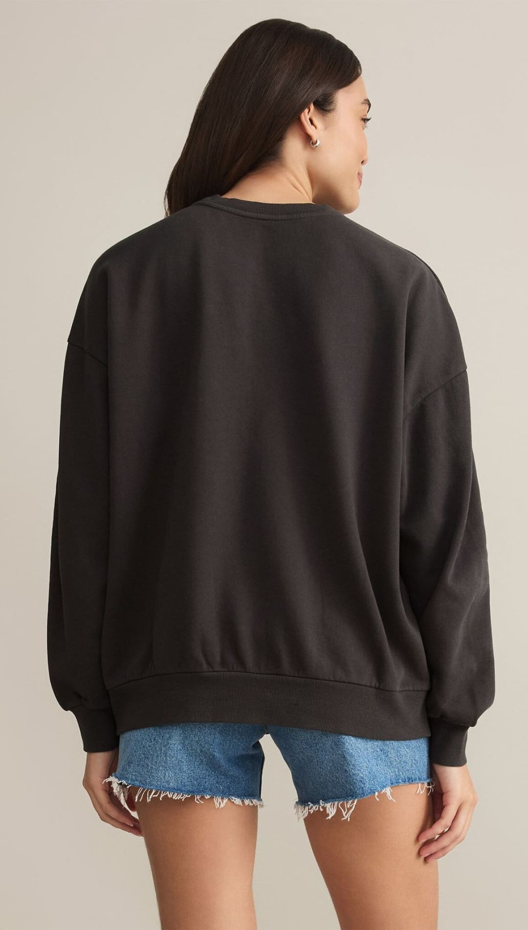 A woman modeling a loose-fitting, dark-colored long-sleeved sweatshirt paired with distressed blue denim shorts.