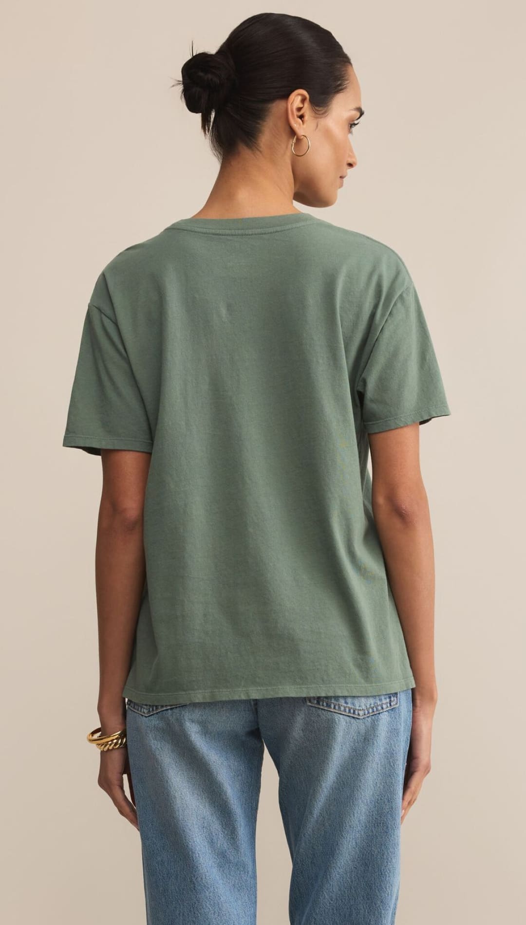 Woman wearing a sage green crewneck t-shirt and blue jeans.