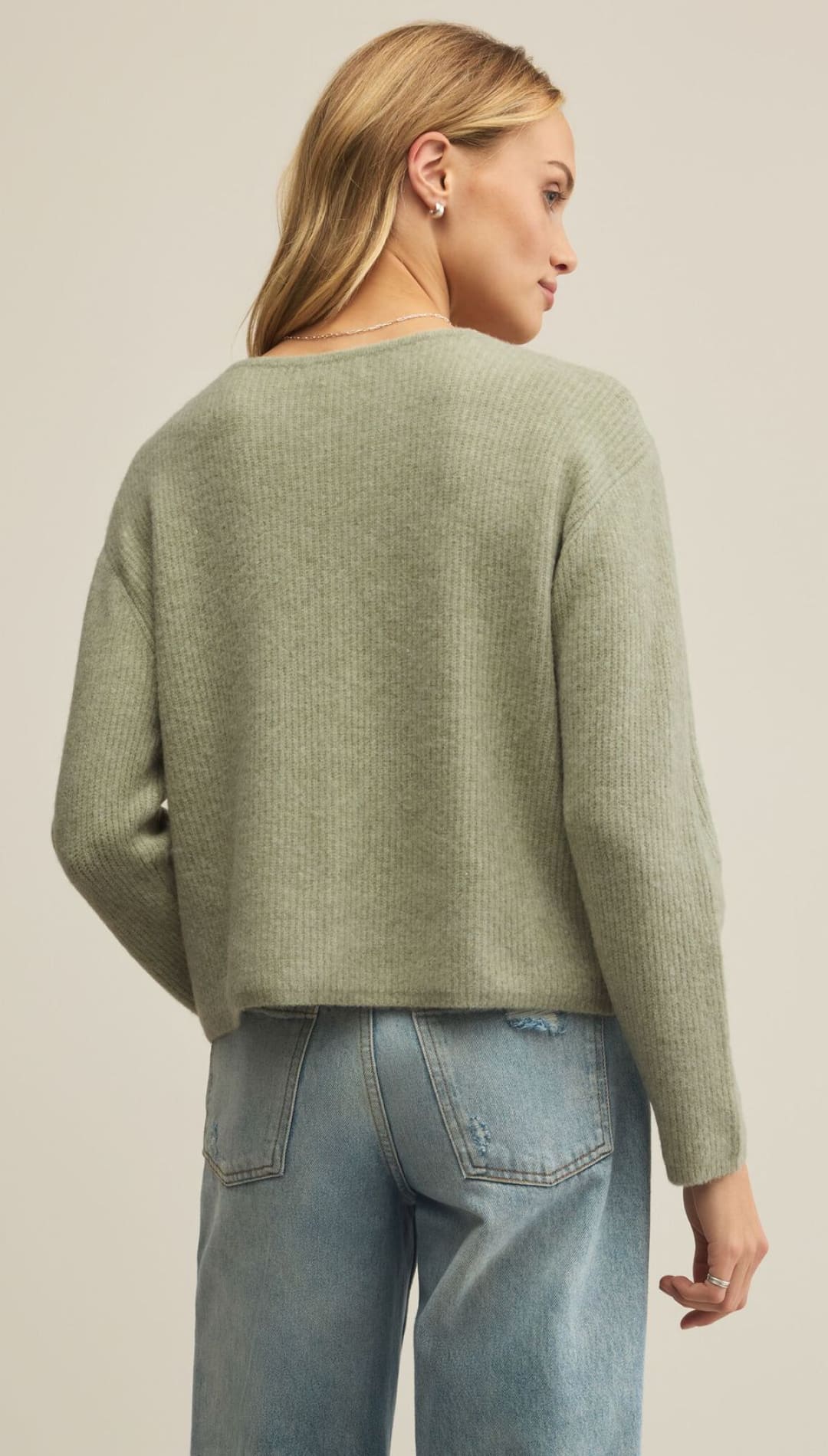 Woman in a sage green crewneck sweater and light wash jeans.