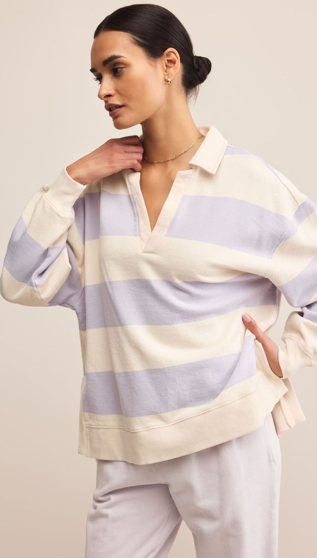 A woman wearing a lavender and cream striped long-sleeved collared shirt with a V-neck and light purple pants.