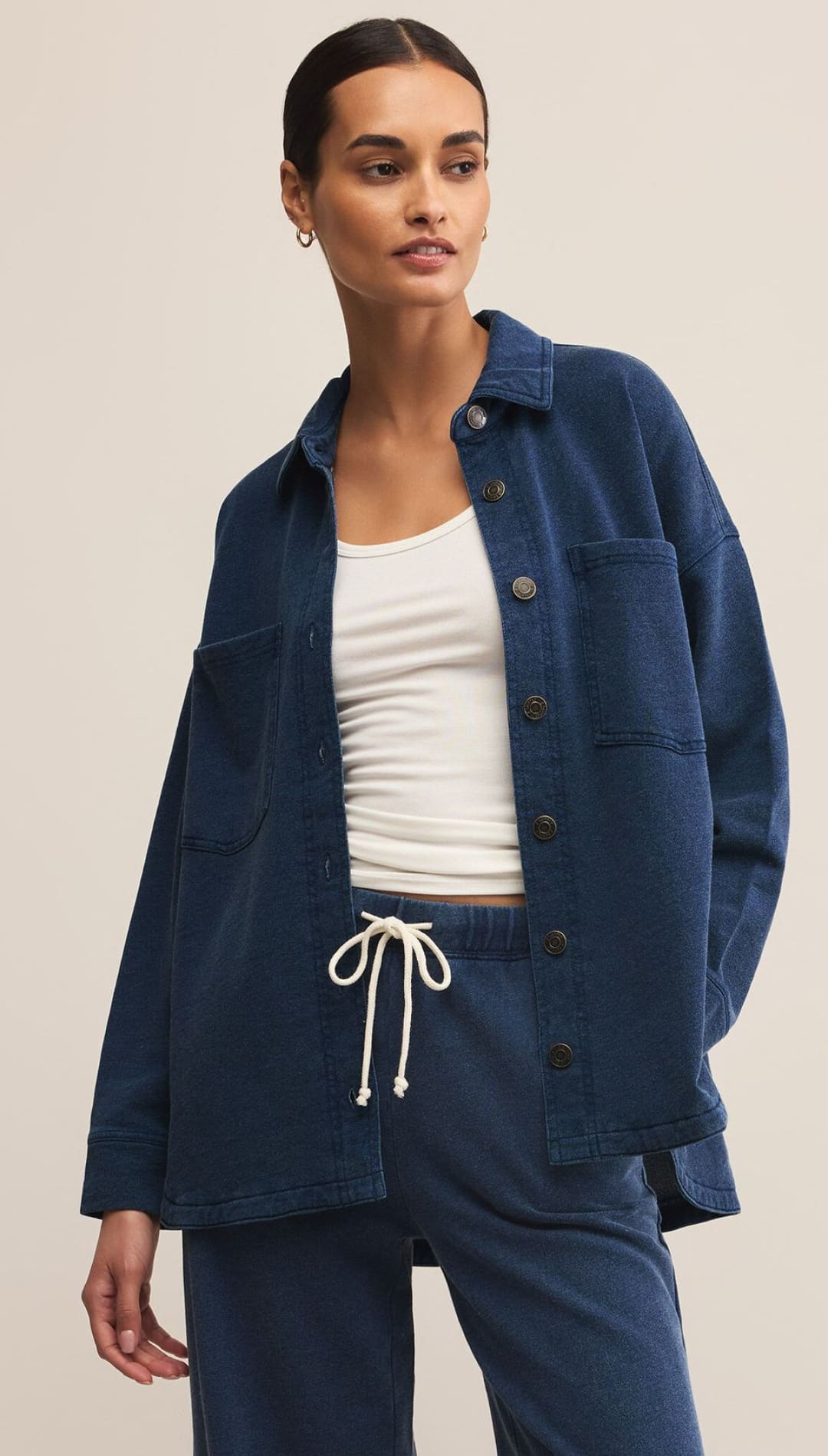 A woman wearing a dark blue button-down shirt-jacket over a white tank top, paired with matching dark blue sweatpants with a white drawstring.