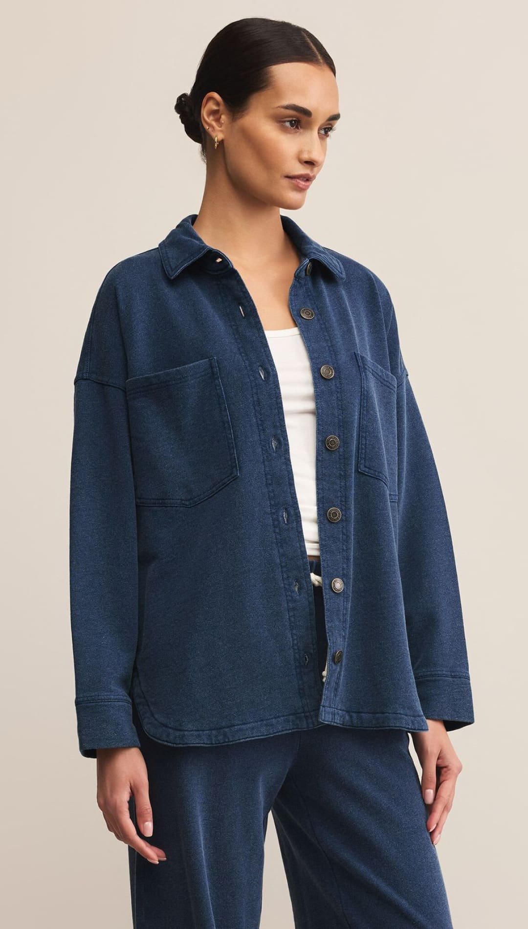 A woman models a relaxed-fit, dark blue button-up shirt jacket with patch pockets, paired with matching trousers.