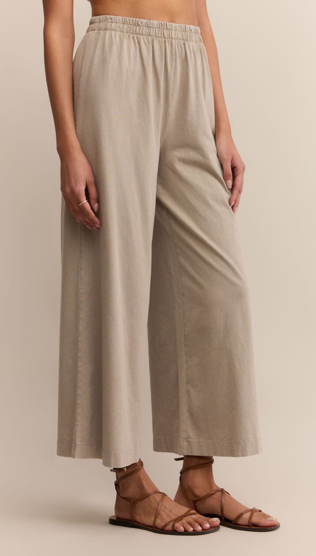 Loose-fitting, light beige, wide-leg pants with an elastic waistband, paired with brown strappy sandals.