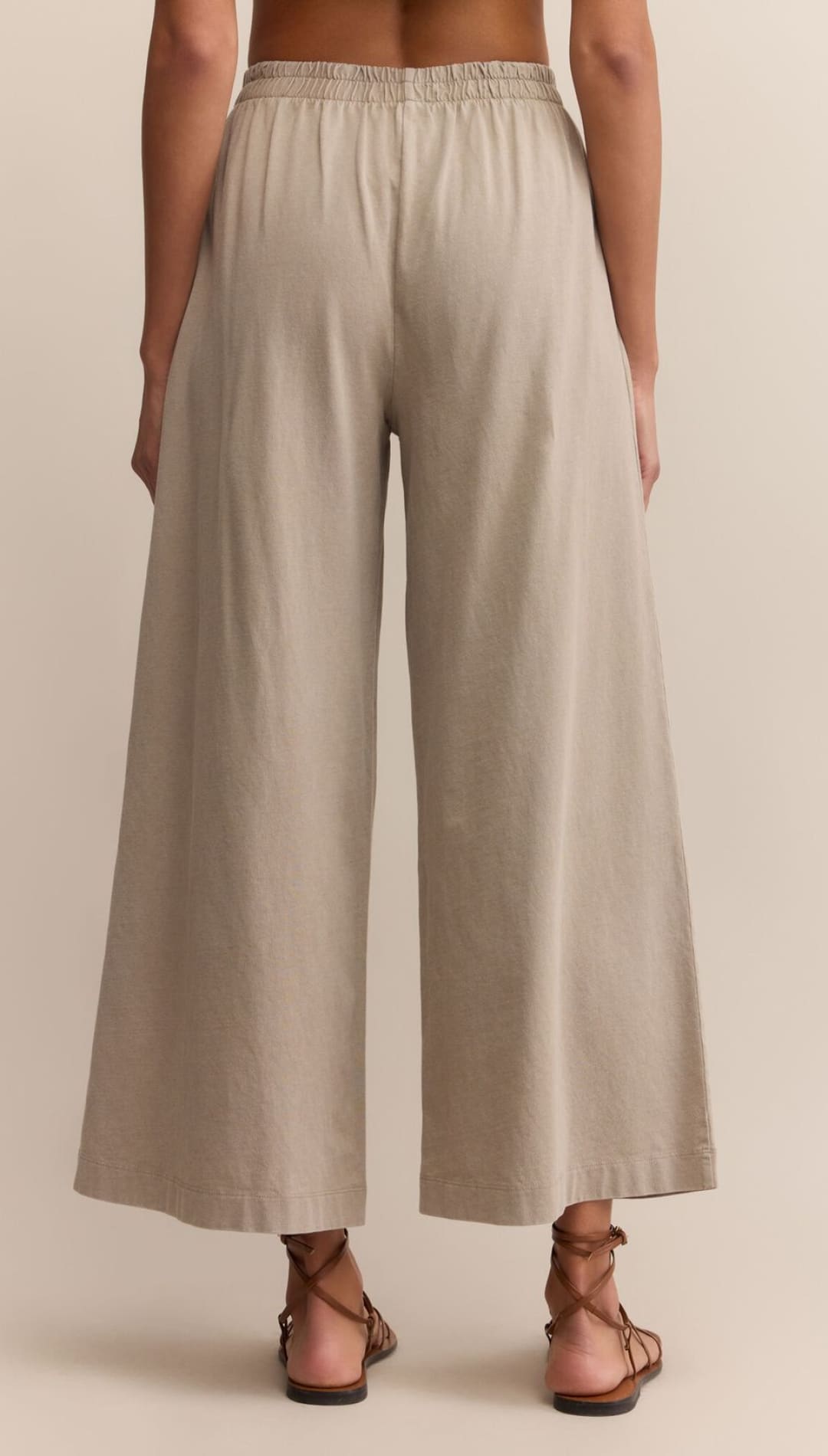 Women’s high-waisted, wide-leg beige culottes with an elastic waistband, paired with brown lace-up sandals.