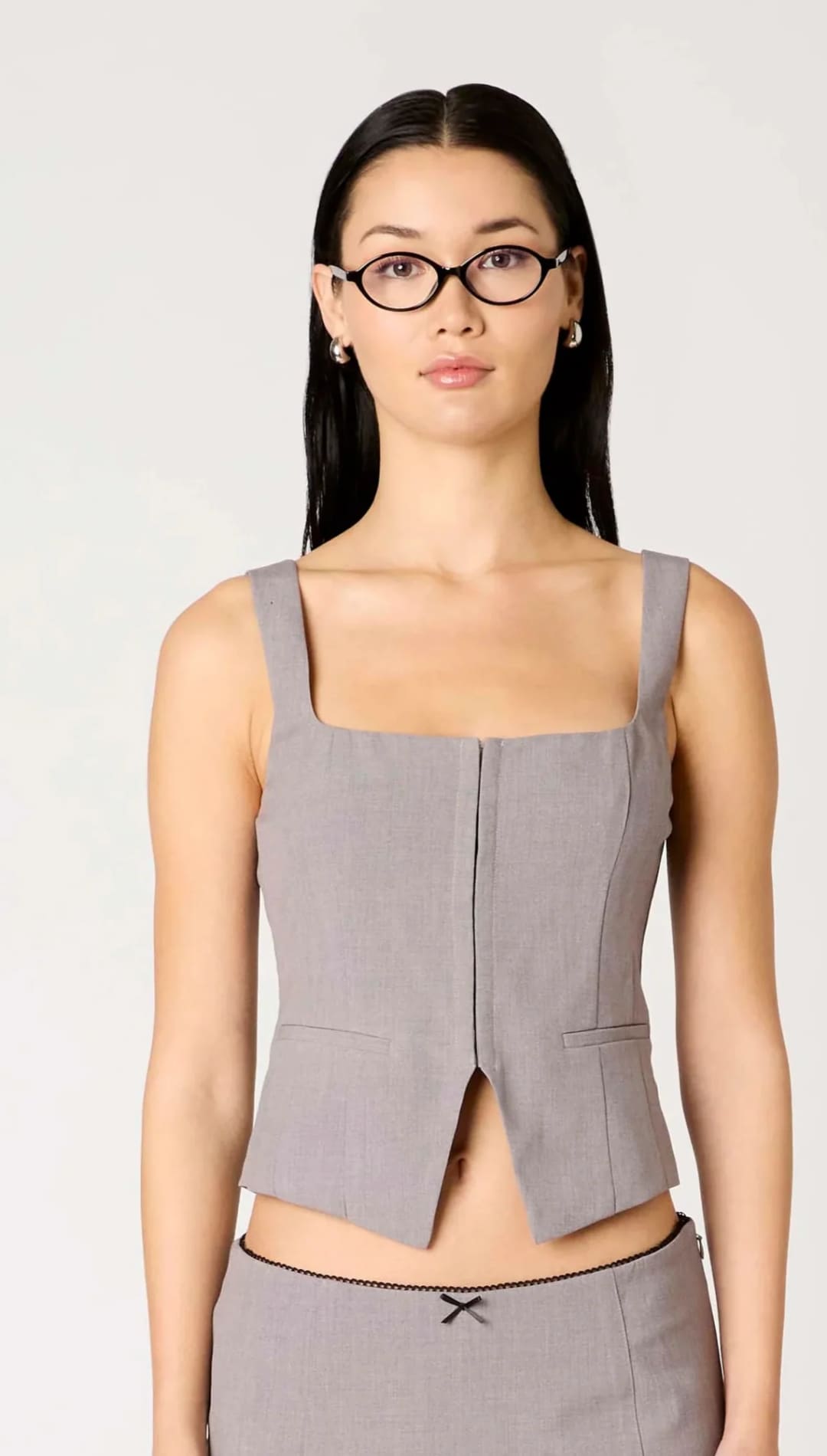 A woman wearing a gray sleeveless crop top and matching mini skirt with a black bow detail.